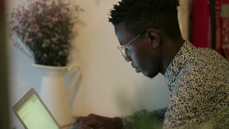 Hombre-Afroamericano-Enfocado-Escribiendo-En-Una-Computadora-Portátil-En-Un-Café